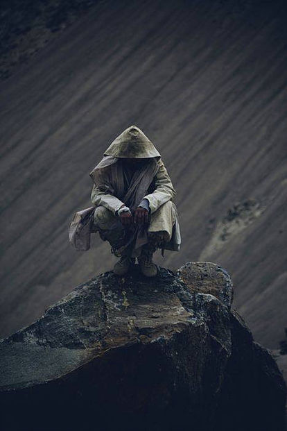 hombre agachado bajo la lluvia y cubierto con un chubasquero y capucha, no se le ve el rostro